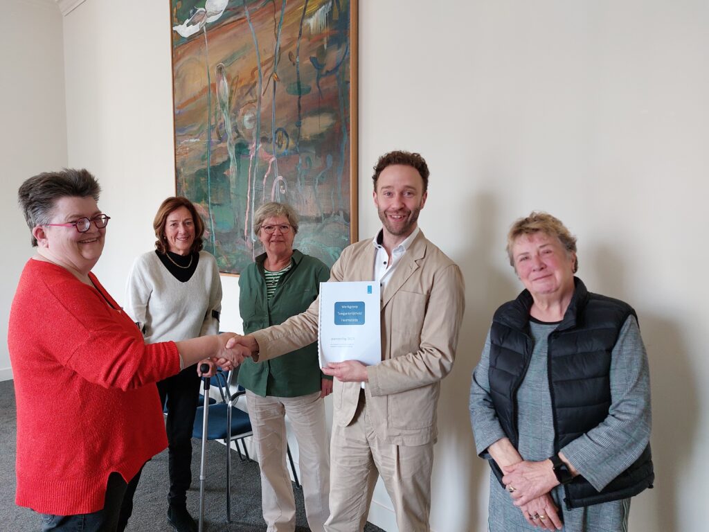 de werkgroep leden en de wethouder. De voorzitter overhandigt het verslag
