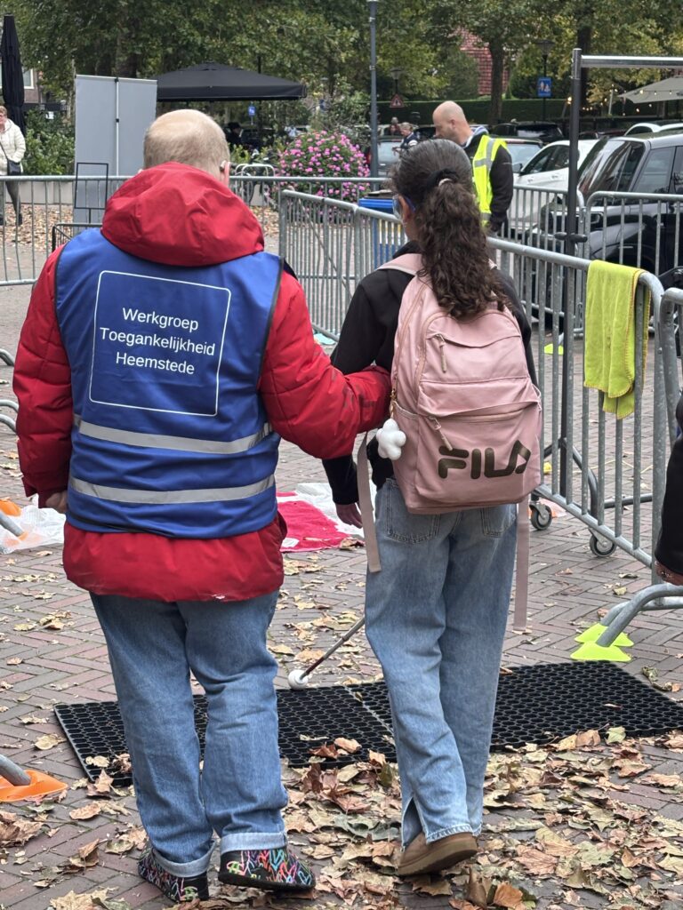 Een vrijwilliger en een vrouw met simulatiebril op in het parcours
